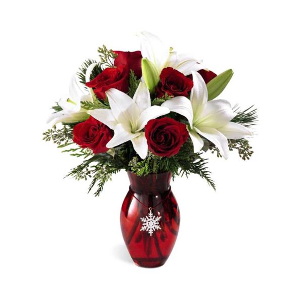 Un arrangement opulent de roses rouges chatoyantes et de magnifiques lys  blancs sont arrangés avec de l'eucalyptus et de la verdure de Noël.